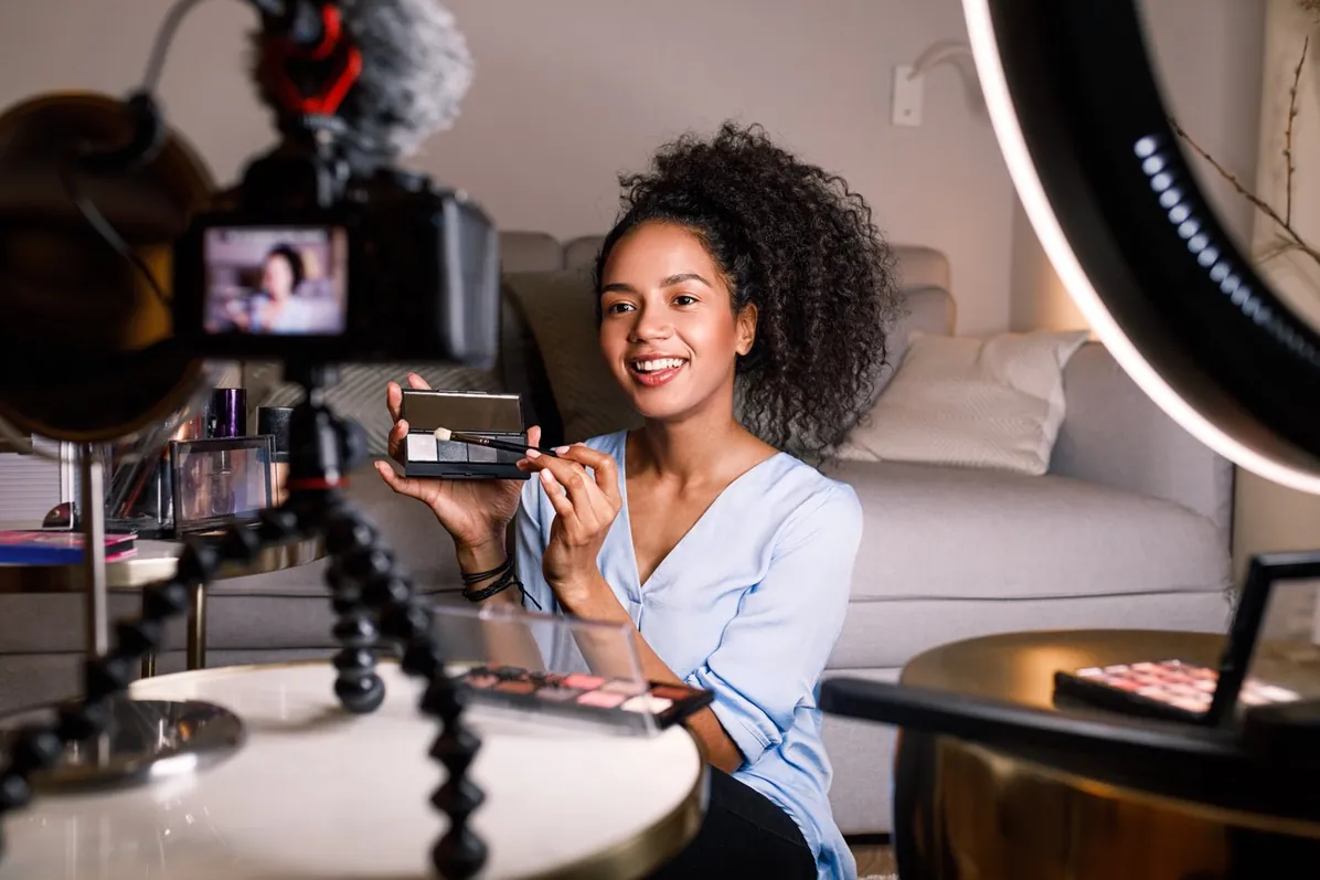 Christine, the content creator: a young woman filming a makeup tutorial at home, holding an eyeshadow palette up to the camera